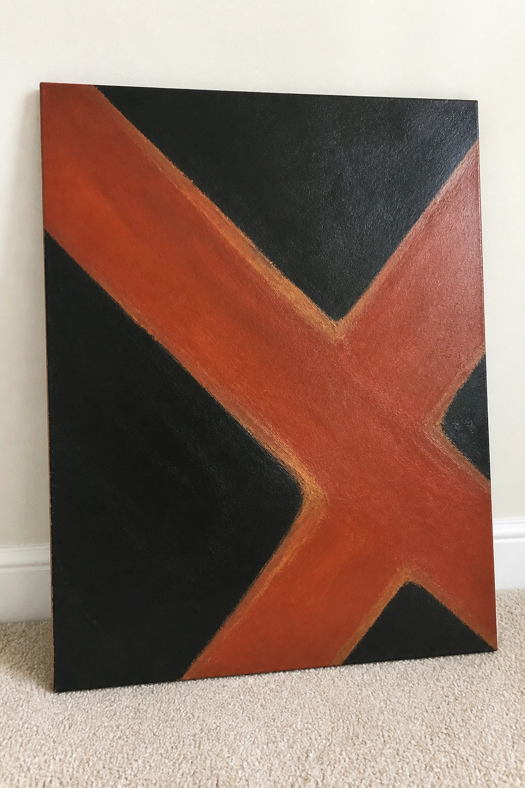 Abstract canvas with bold black and rust-orange diagonal X brushstrokes leaning on carpeted floor