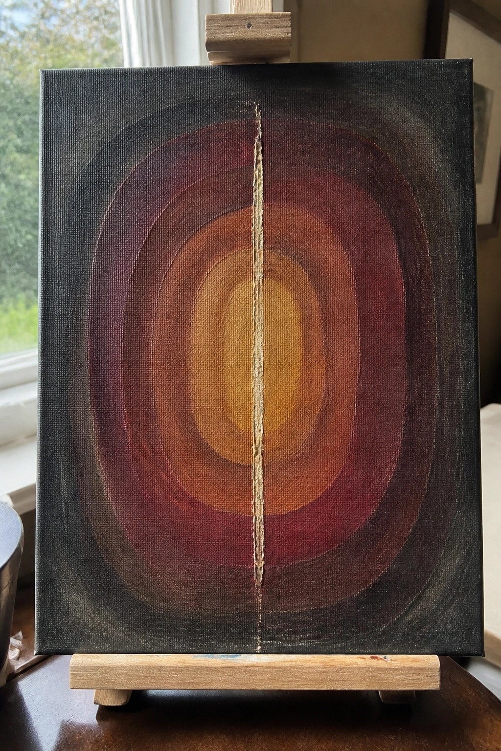 Abstract canvas on easel with concentric red-orange ovals and central gold vertical line.