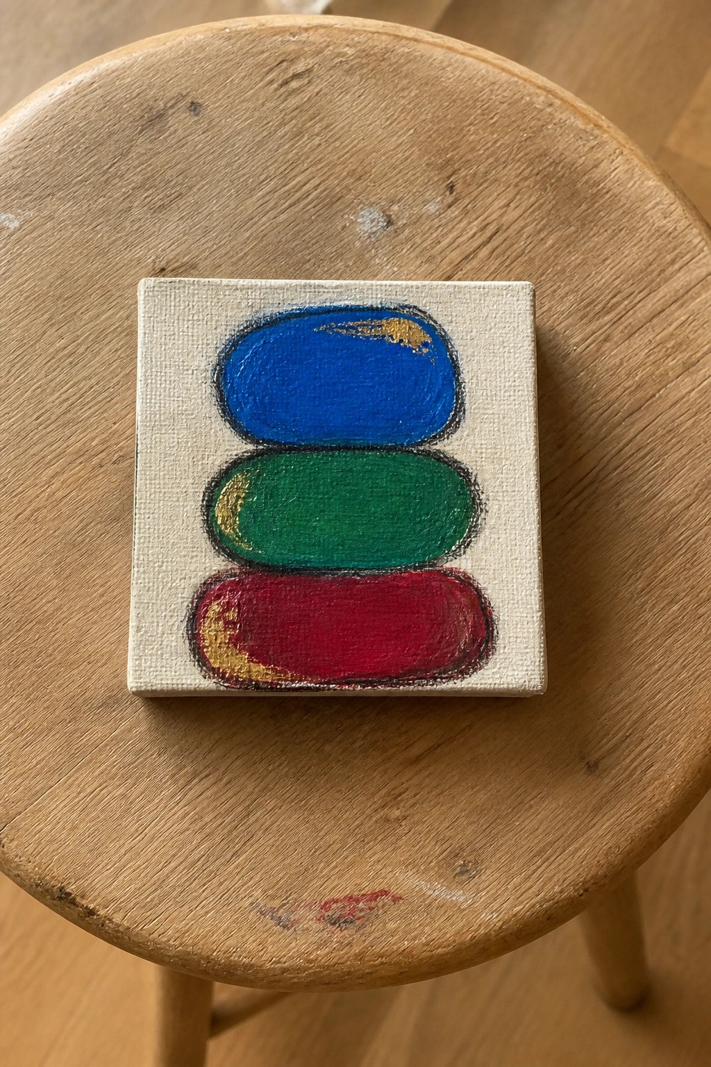 Three stacked blue green and red ovals on a small canvas atop wood.