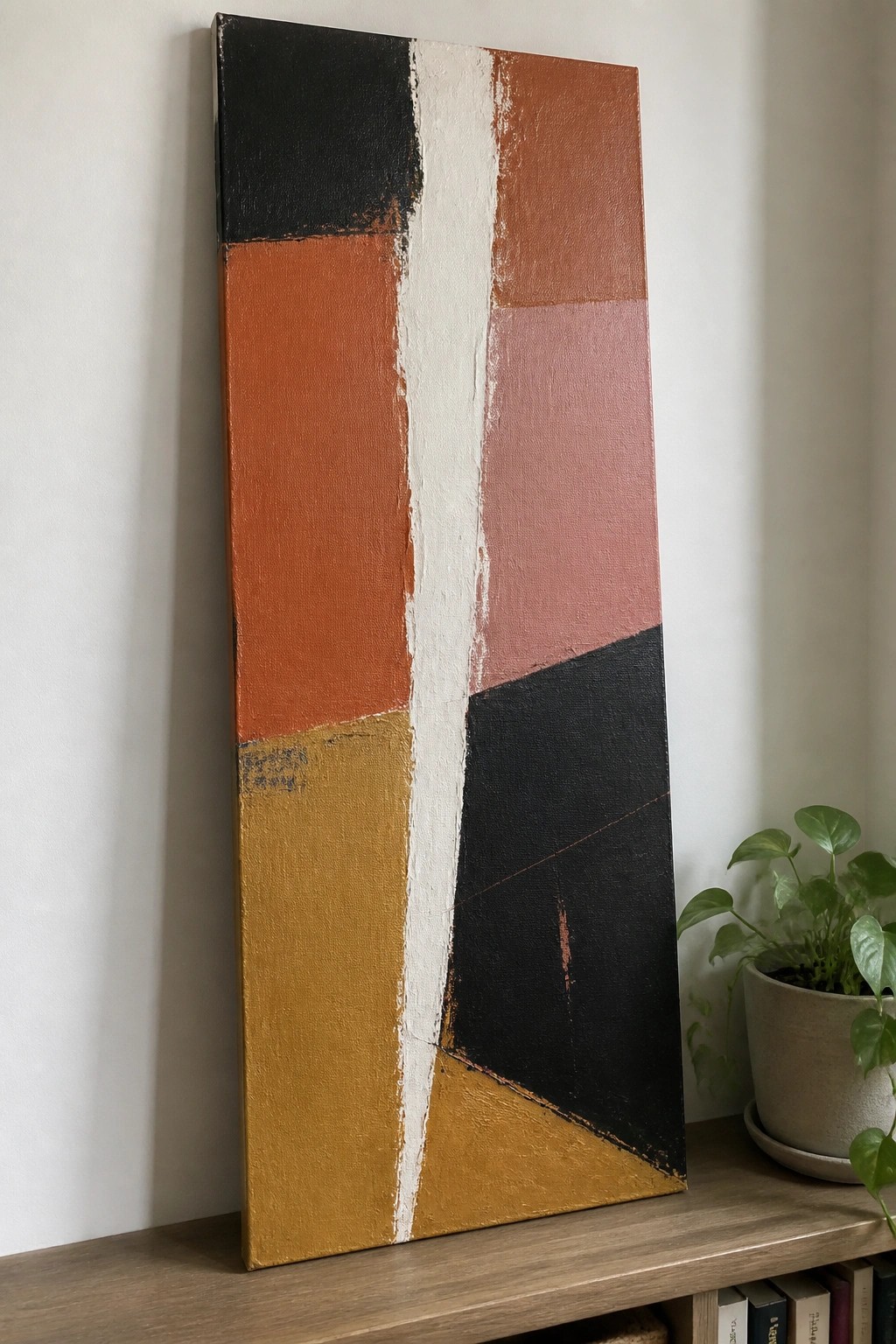 Abstract painting with geometric blocks of black, orange, yellow, pink, and white beside plant