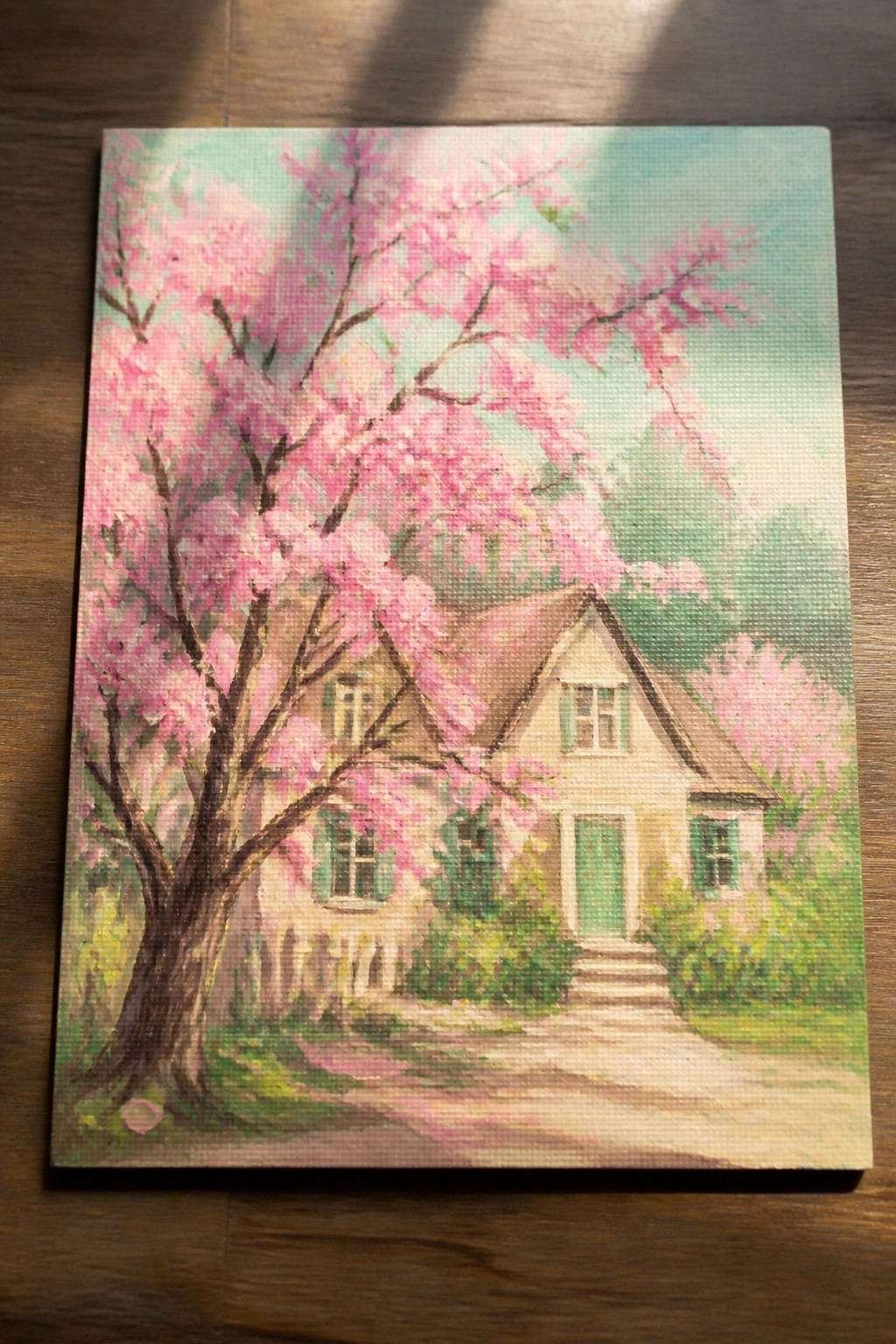 Painting of cottage with blooming pink tree, green door and winding path.