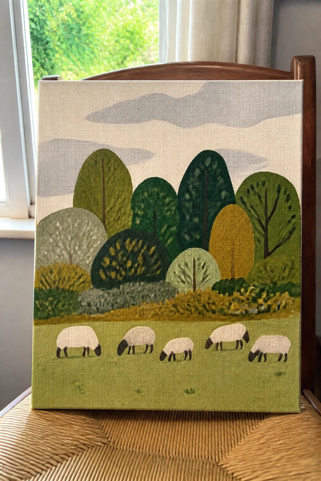 Stylized landscape painting with green trees, clouds, and five grazing sheep on canvas.