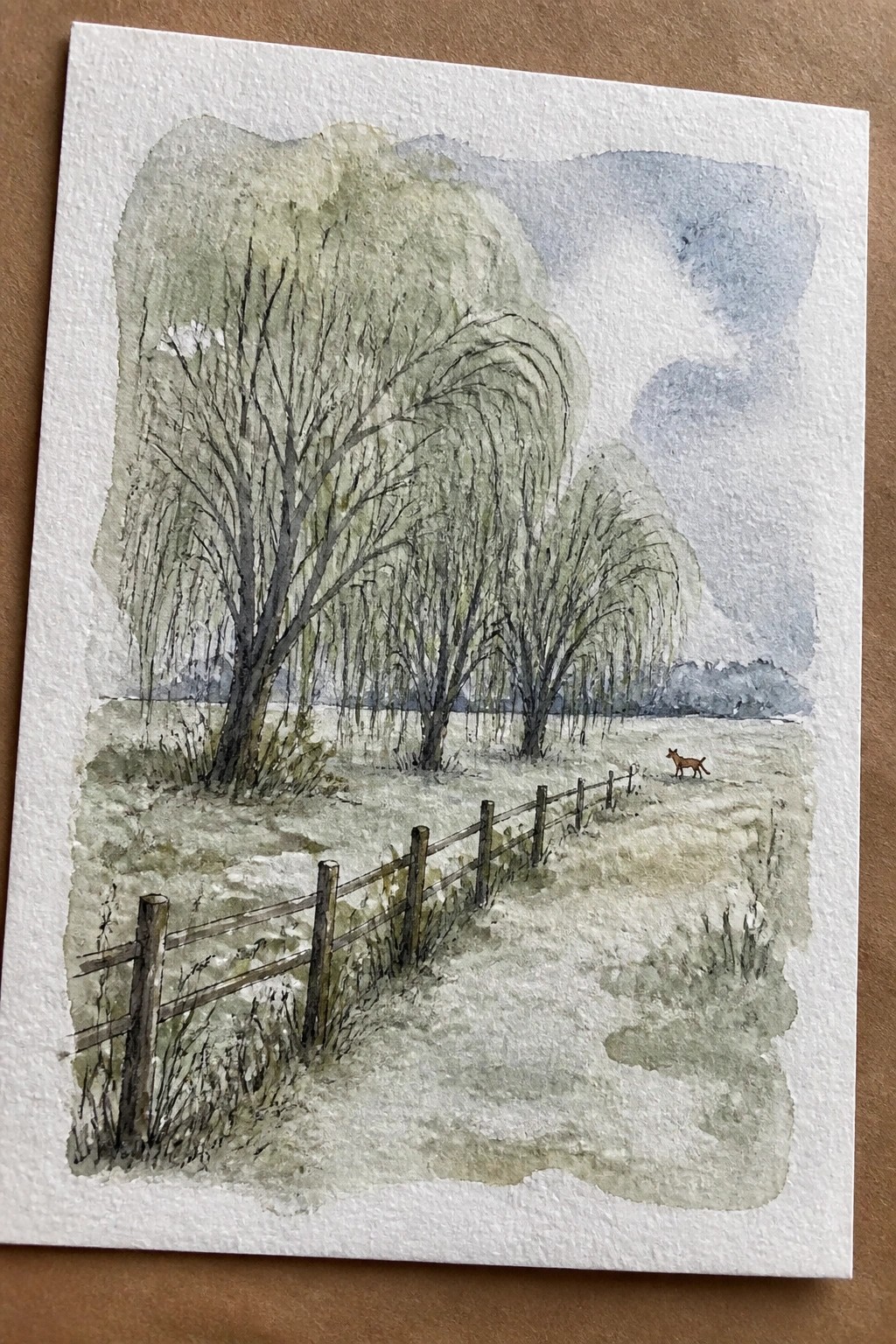 Watercolor of willow trees, wooden fence, and fox in open field under cloudy sky