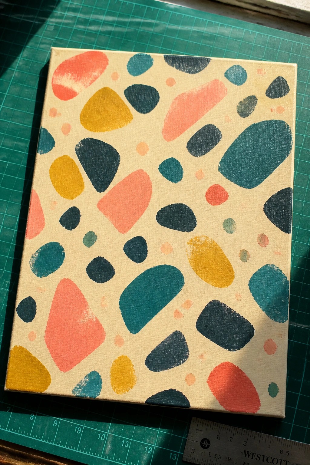 Abstract canvas with colorful pebble shapes in coral teal yellow on green cutting mat
