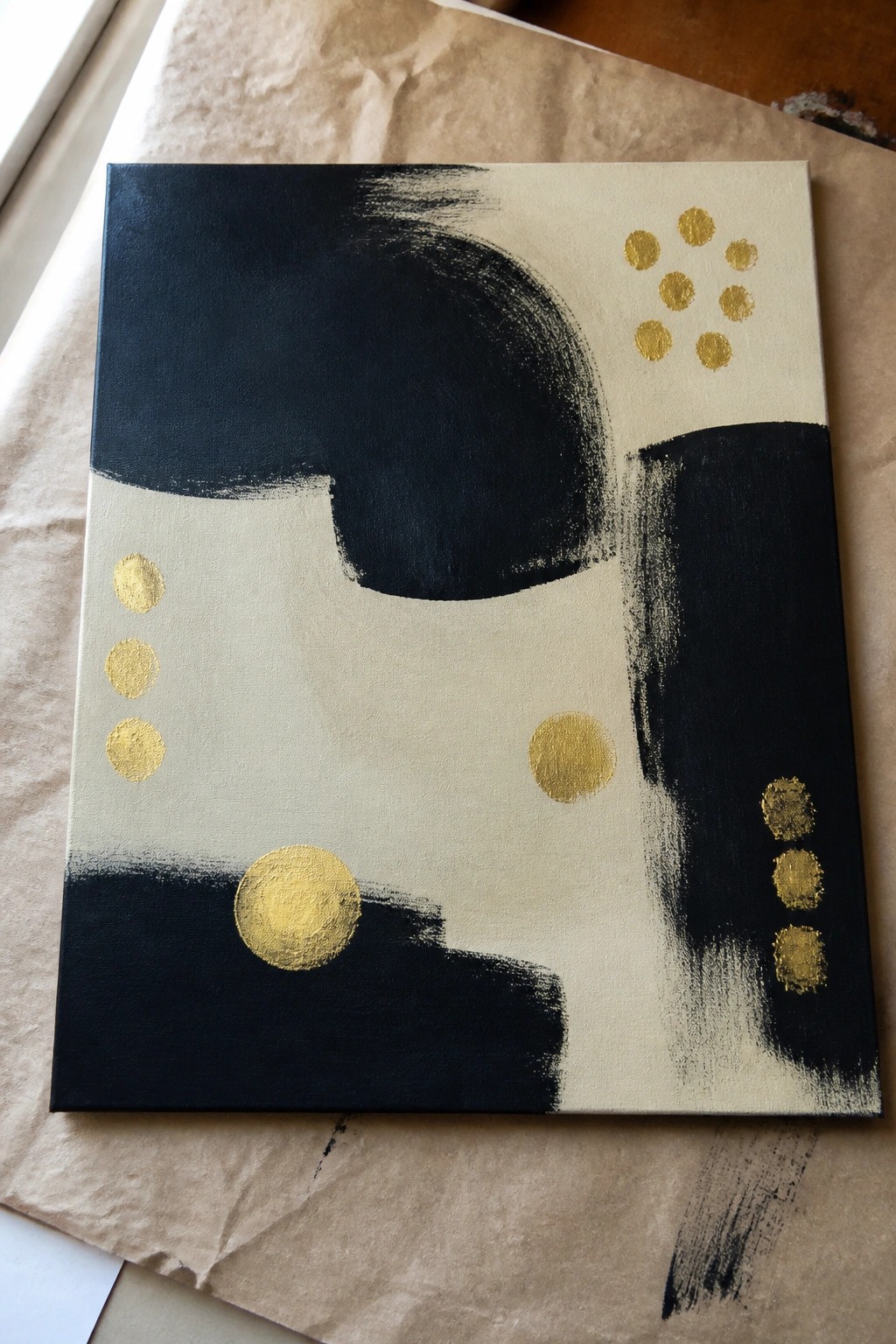 Abstract painting with black brushstrokes, gold dots on cream and black canvas