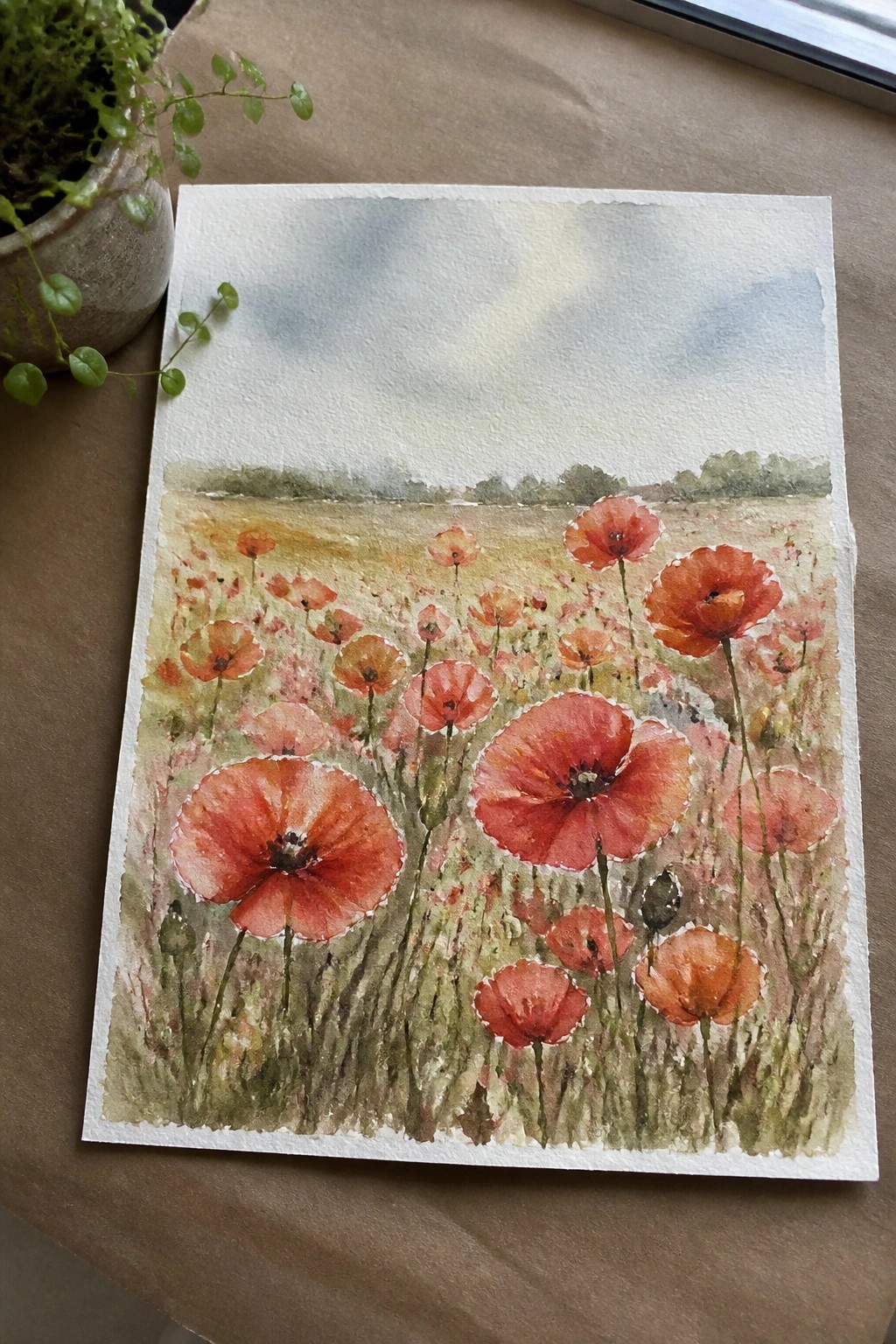 Watercolor of red poppies blooming in a grassy field under a cloudy sky