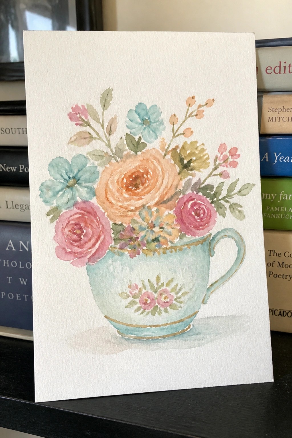 Watercolor of pink and peach roses in a light blue teacup with gold trim