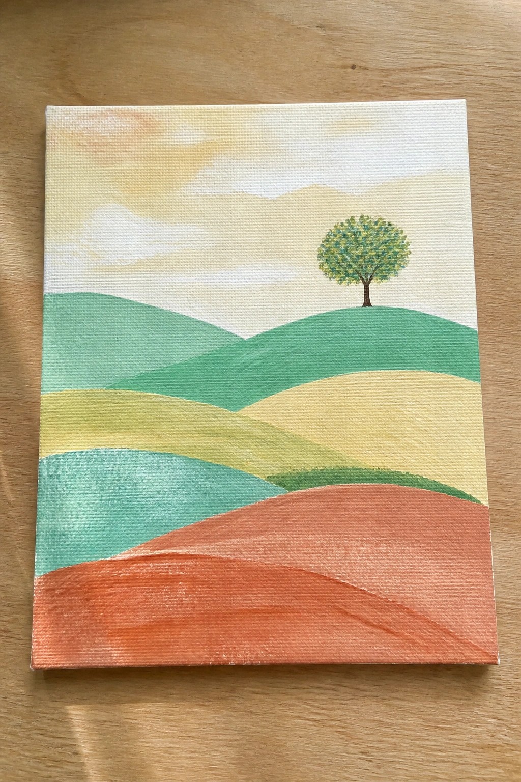Landscape painting of rolling hills in orange teal yellow green with lone tree and soft sky.