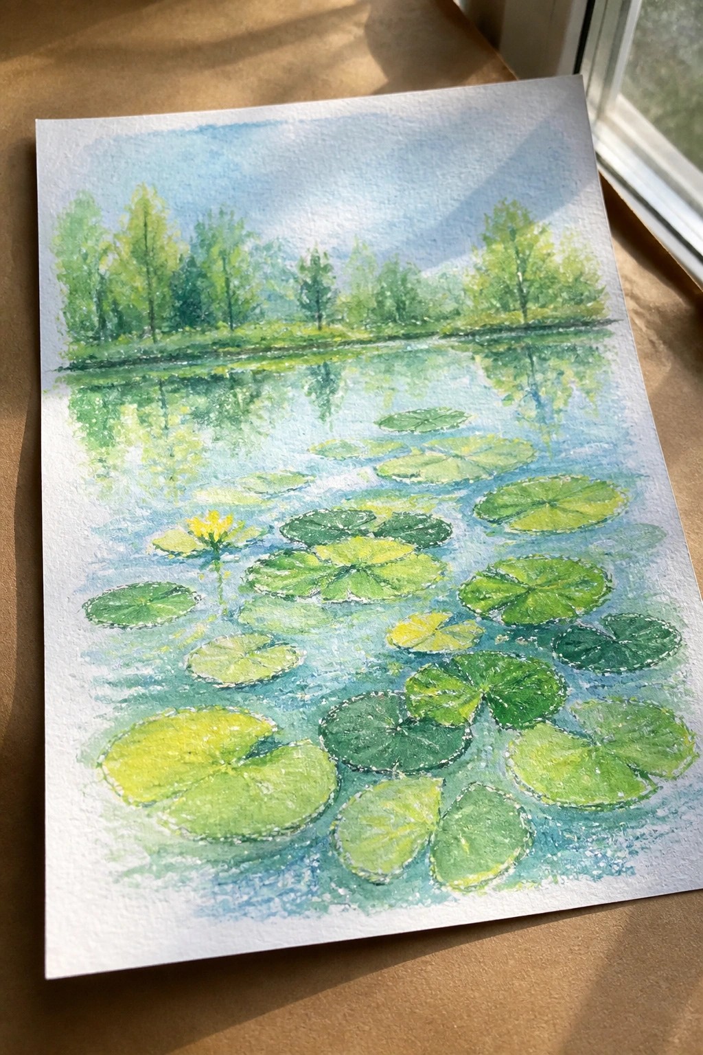 A watercolor painting of a pond with green lily pads of different sizes, one yellow flower, and reflections of trees on the water.