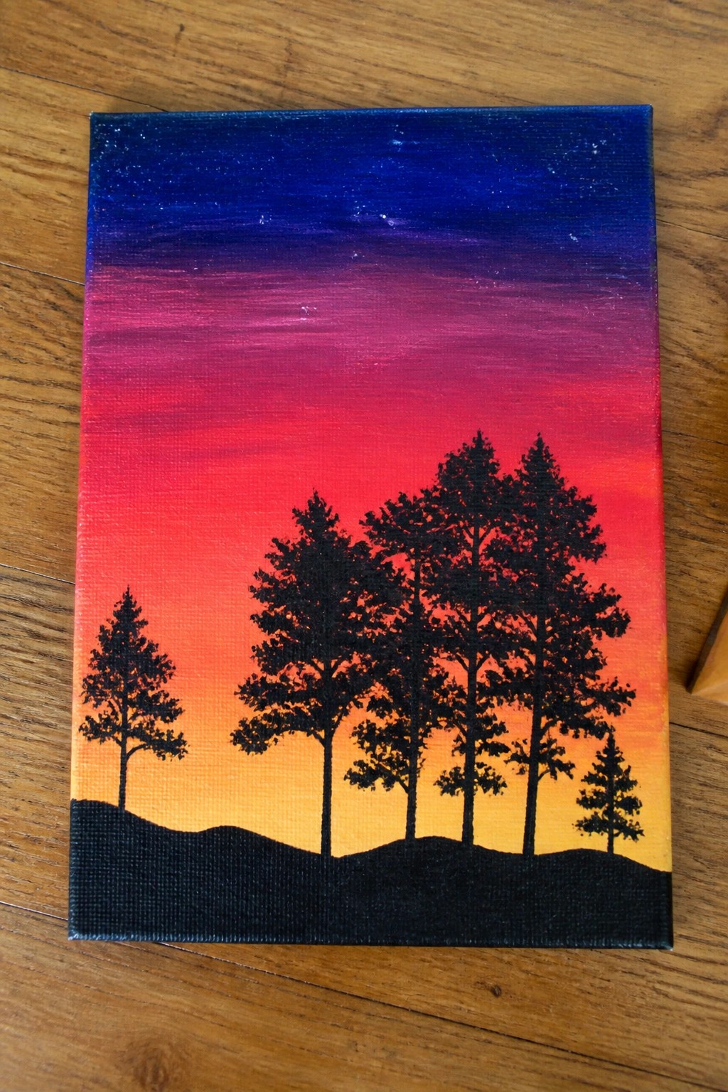 A canvas shows a gradient sky from blue to orange with black silhouetted pine trees on a dark hill.