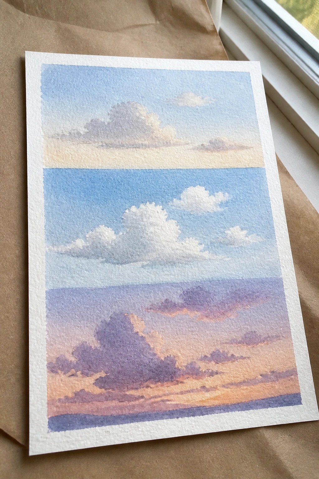 Three watercolor sky panels showing daytime clouds above a purple-orange sunset.