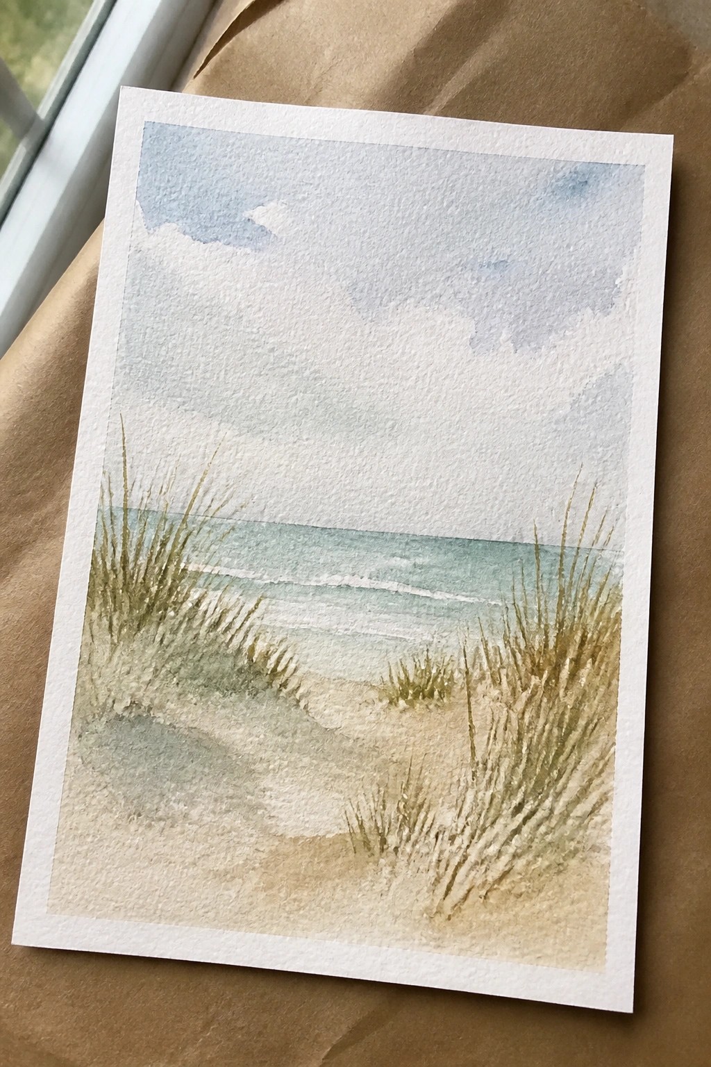 Watercolor beach scene with sandy dunes, sea grass, turquoise waves, and cloudy sky