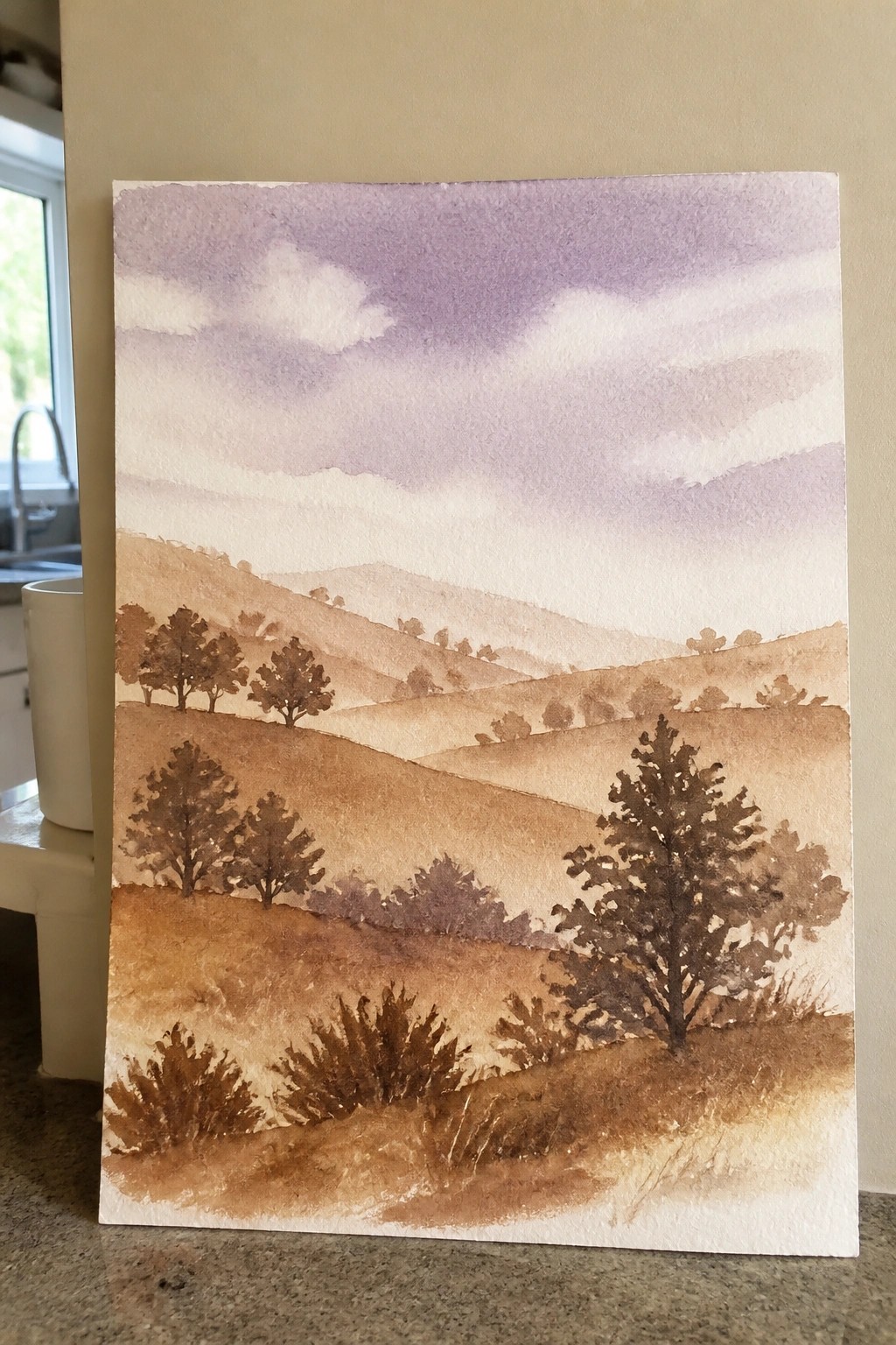 Watercolor landscape of rolling brown hills dotted with trees beneath a purple sky