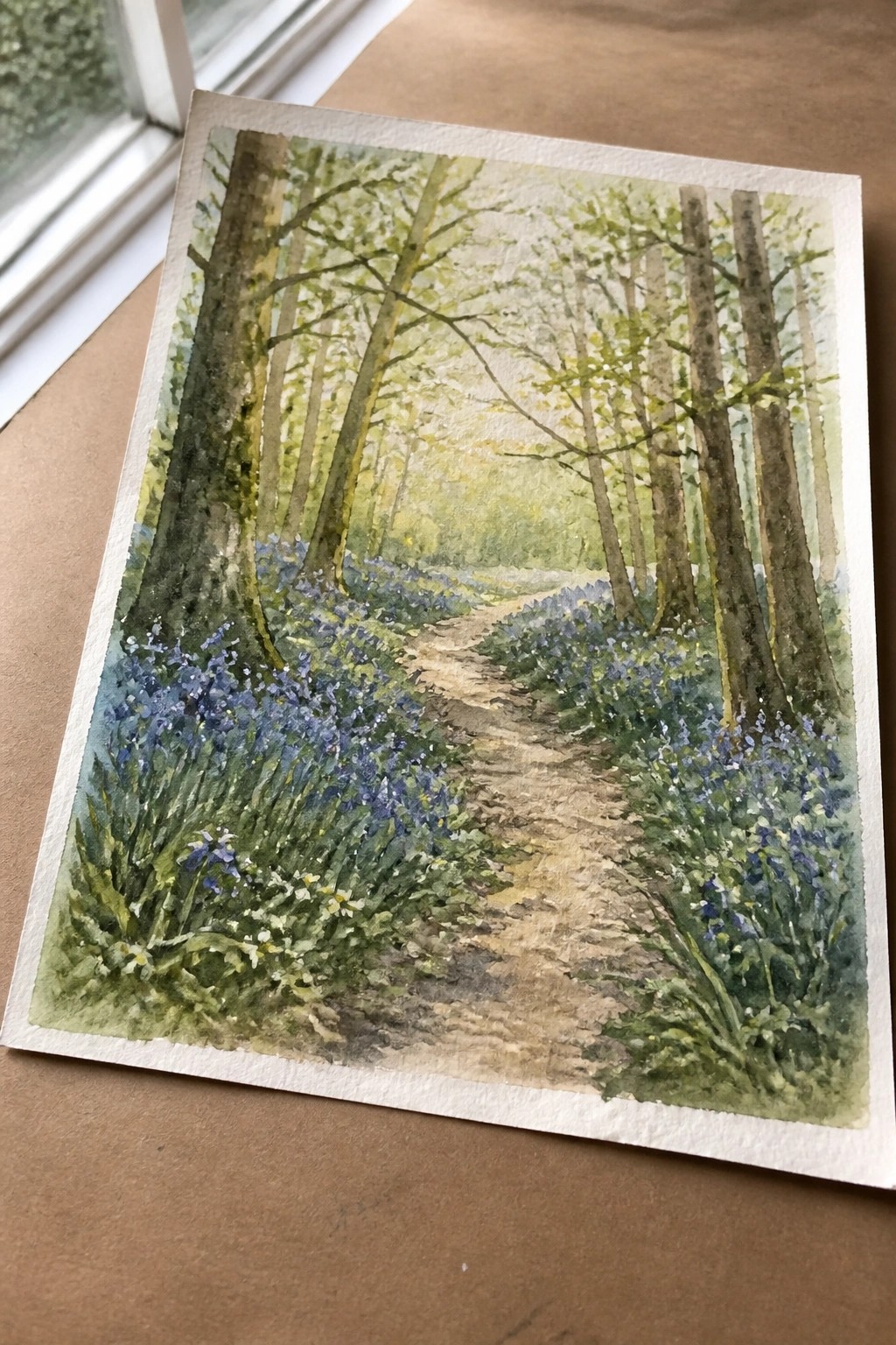 Watercolor painting of a sunlit forest path lined with bluebells and tall trees