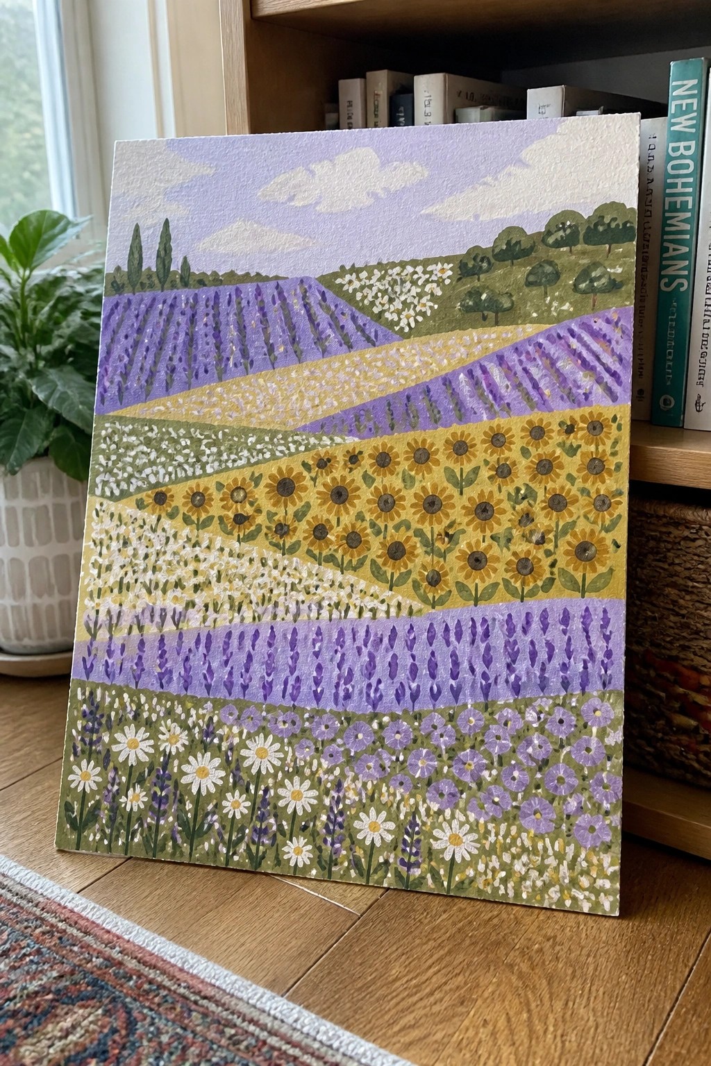 Vibrant landscape painting of flower fields leaning against bookshelf with books