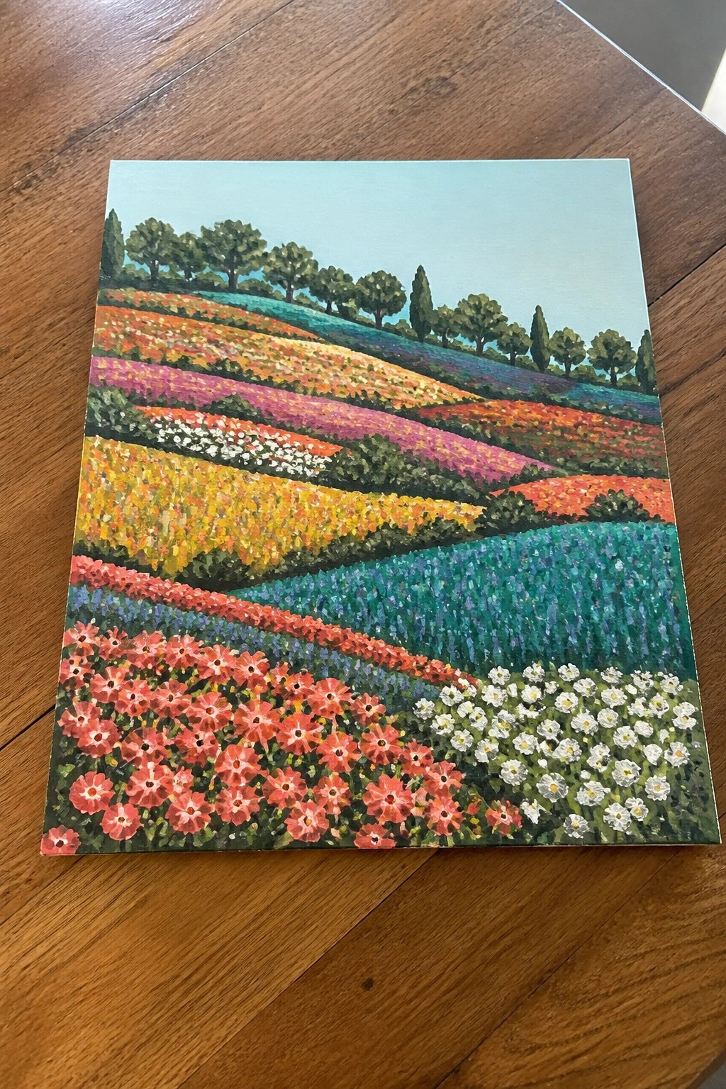 A painting of colorful flower fields arranged in horizontal bands across rolling hills with trees along the horizon.