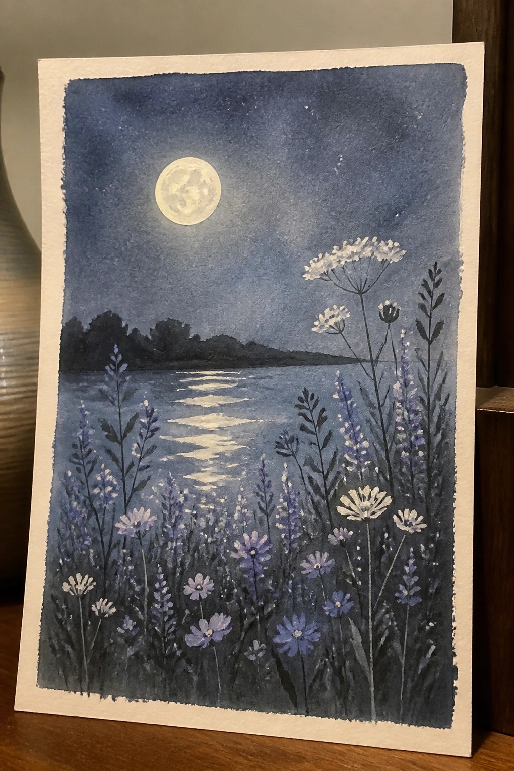 Watercolor night scene of full moon over lake with purple wildflowers.