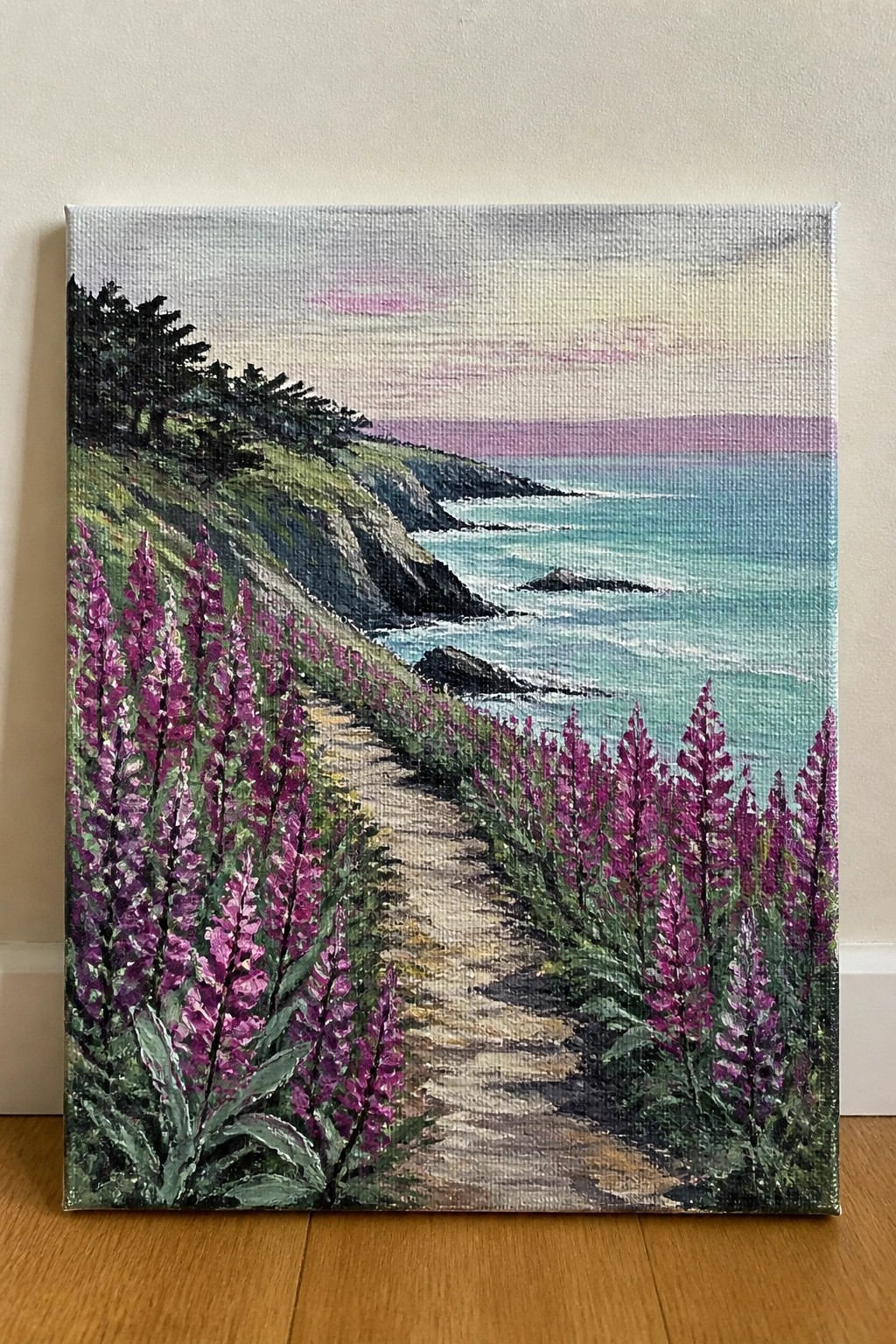 Painting of a winding path lined with purple flowers beside a turquoise sea at sunset.