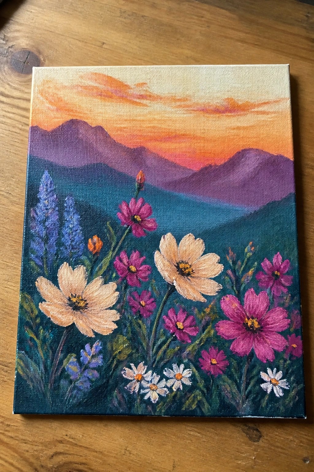 Vibrant painting of pink wildflowers and daisies before purple mountains at sunset