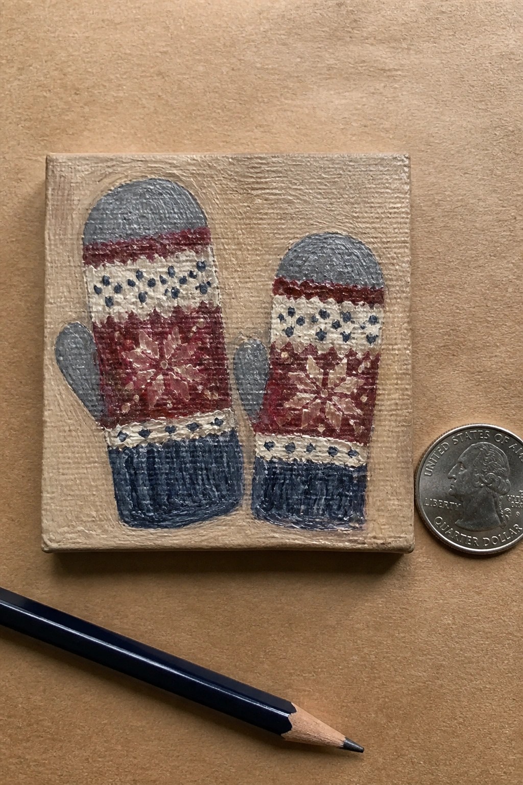 Miniature painting of red, white, and blue snowflake mittens beside quarter and pencil.