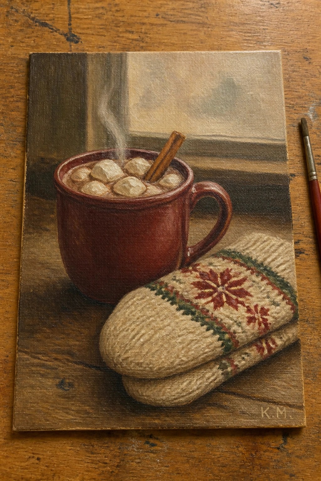 Red mug of steaming cocoa with marshmallows and cinnamon beside patterned knitted mittens on wood.