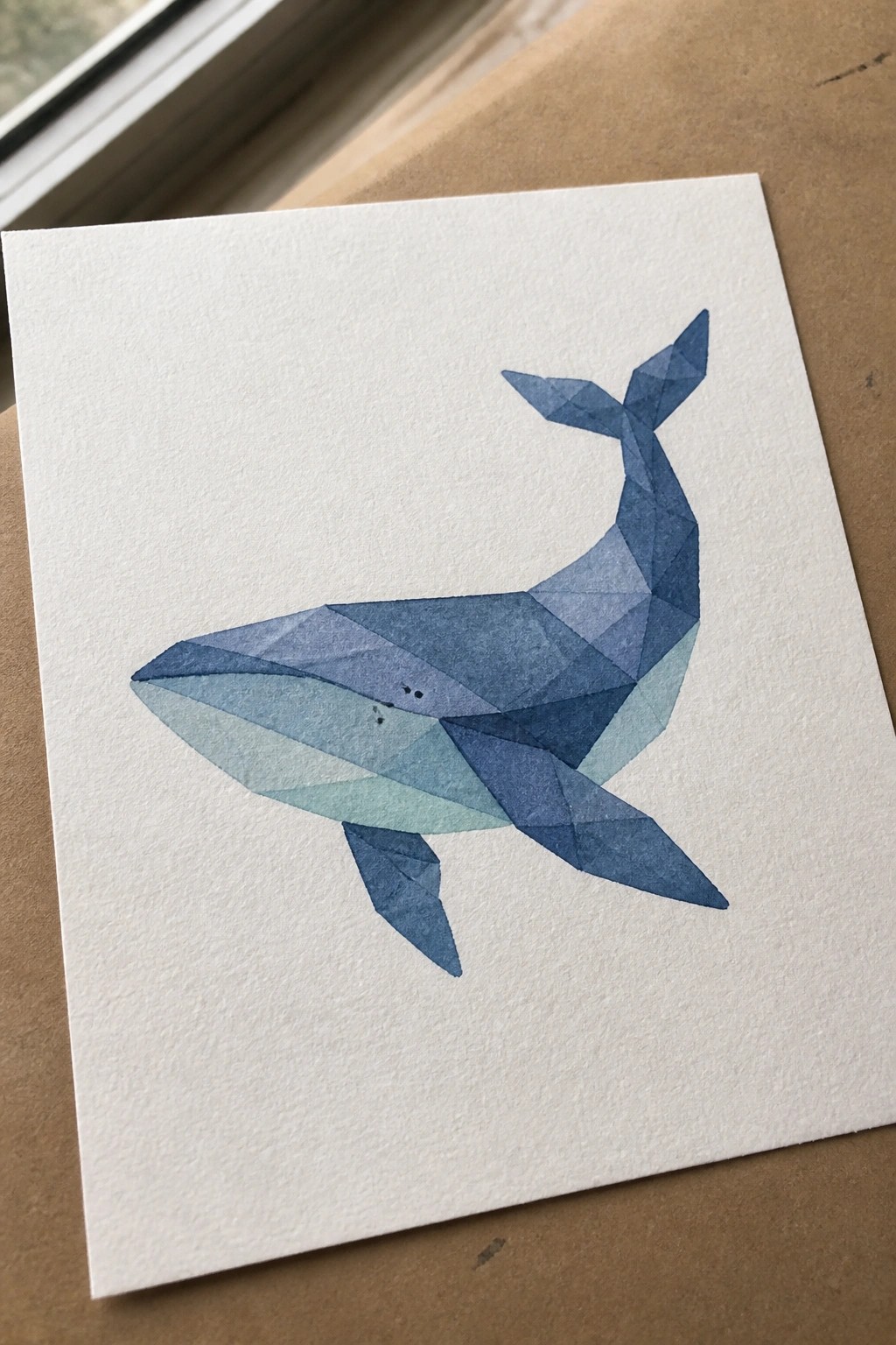 Geometric blue whale formed by overlapping triangles in various shades on white paper