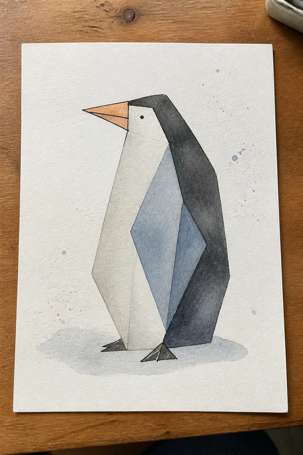 Geometric watercolor penguin with black, white, and blue body plus orange beak on paper