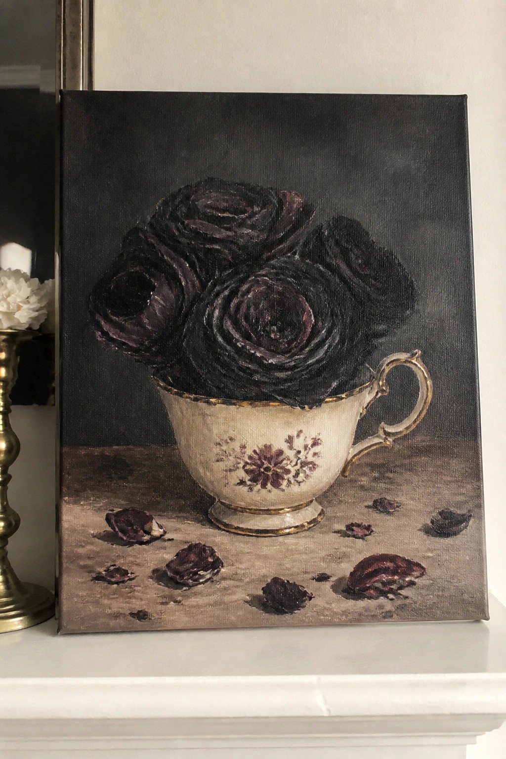 Dark roses fill a gold-trimmed floral teacup with scattered petals on a brown surface.