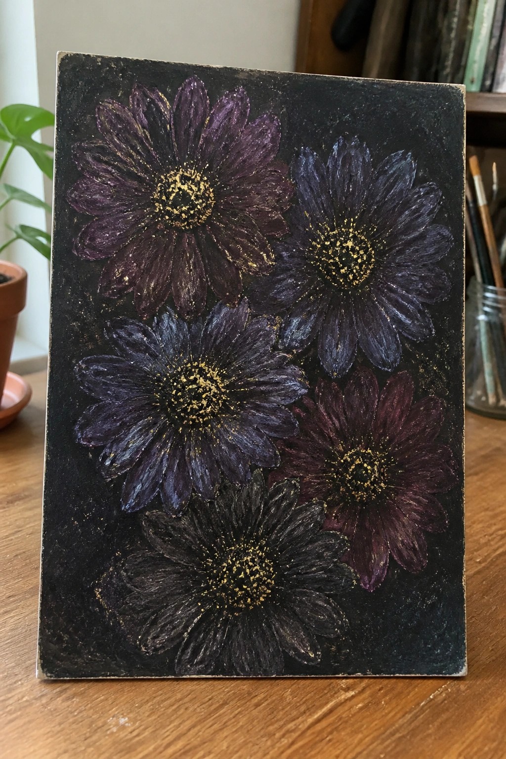 Five dark purple daisies with gold centers on textured black canvas atop wooden table