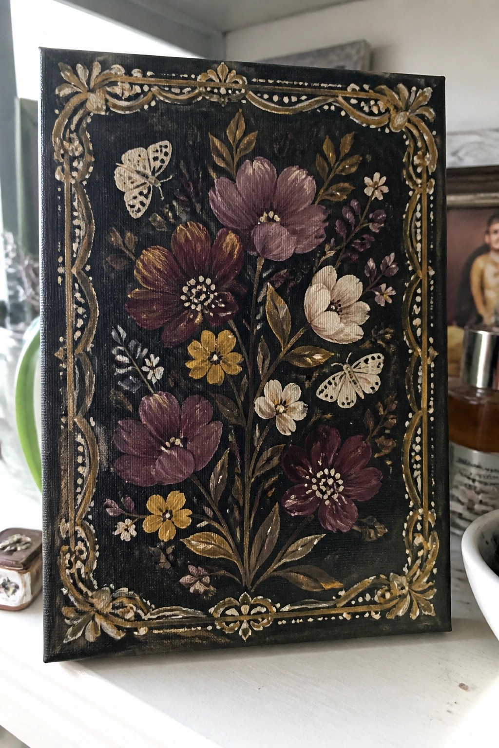 Dark canvas with ornate gold border, purple flowers, and two butterflies
