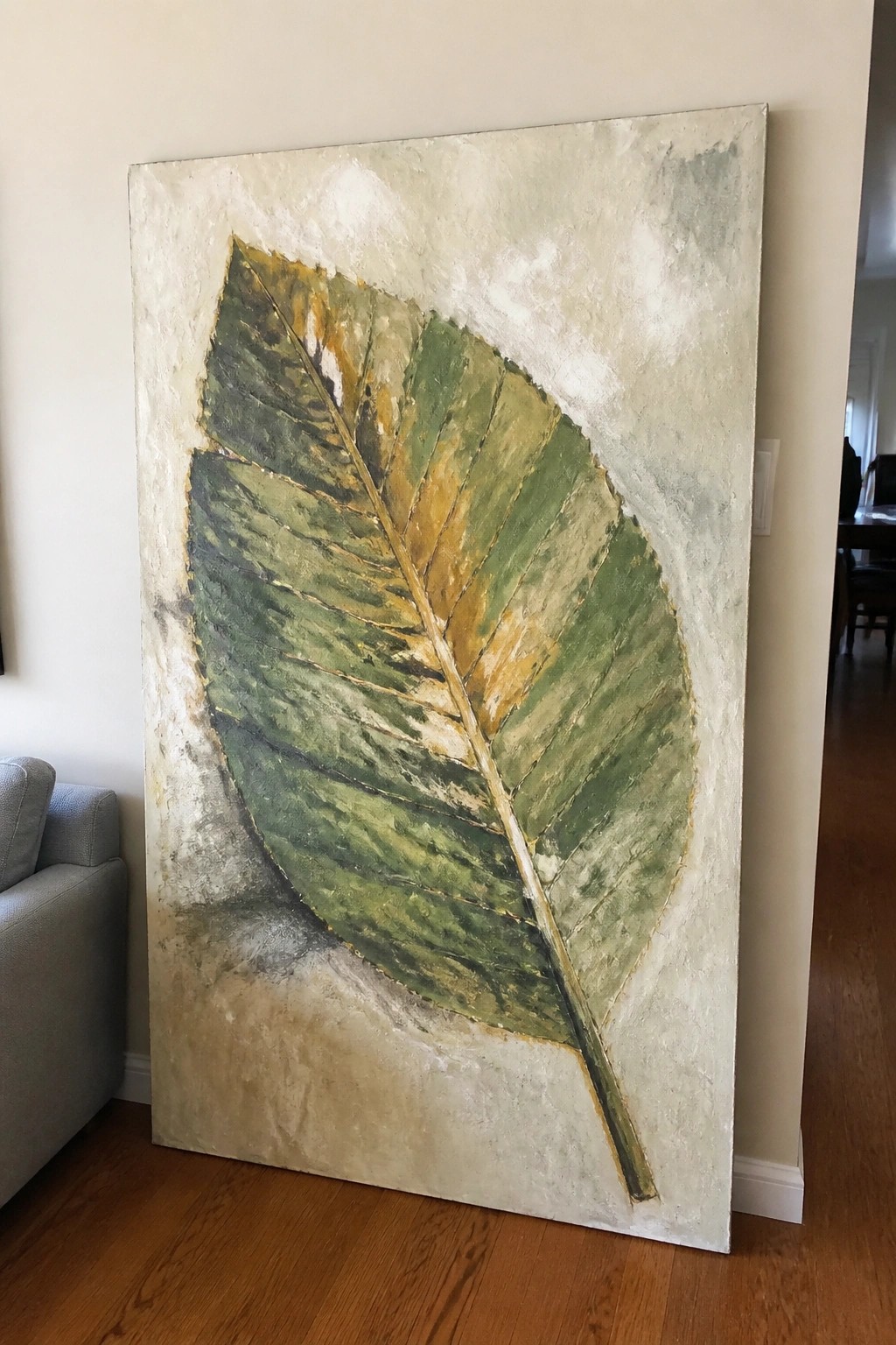 Large textured painting of a green leaf with gold accents leaning on a wall