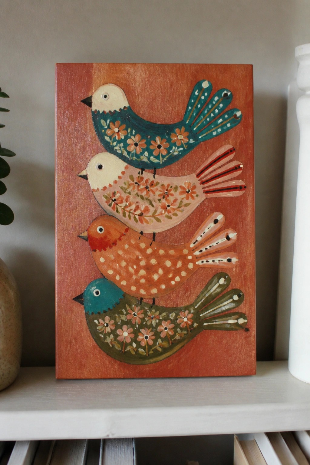 Four stylized birds with floral patterns stacked vertically on a reddish-orange wooden panel.