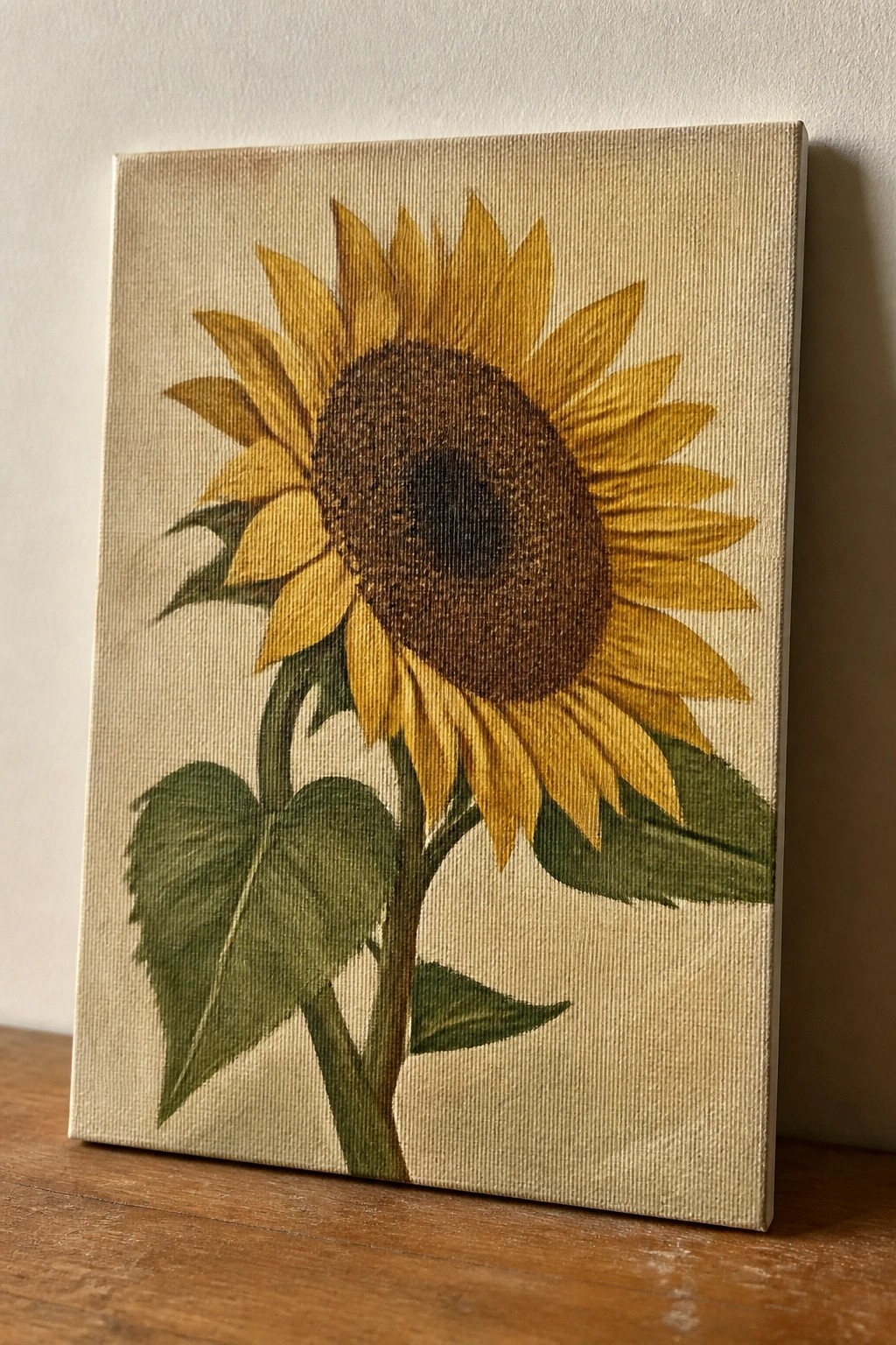Sunflower painting with yellow petals, brown center, and green leaves on beige canvas