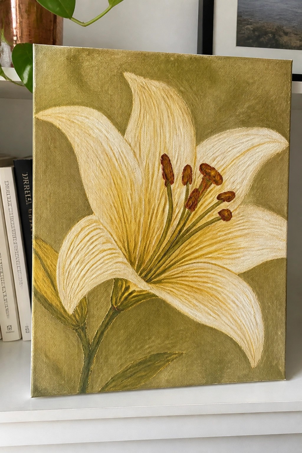 White lily with brown stamens on textured olive-gold canvas beside books.
