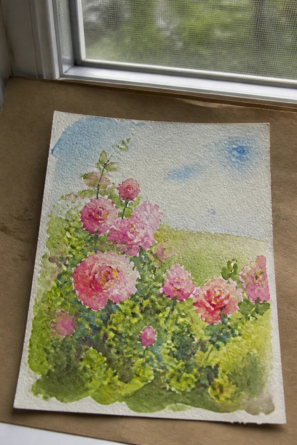 Watercolor painting of pink roses and green foliage beside a window