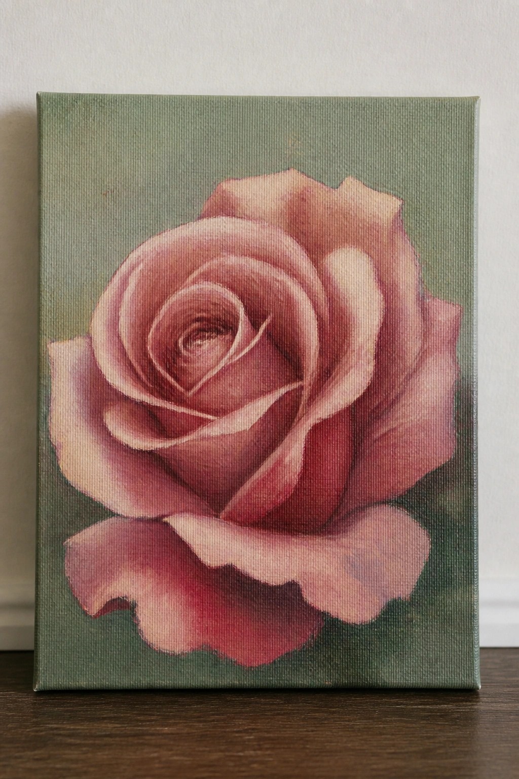 Realistic painting of blooming pink rose on textured green canvas atop wood