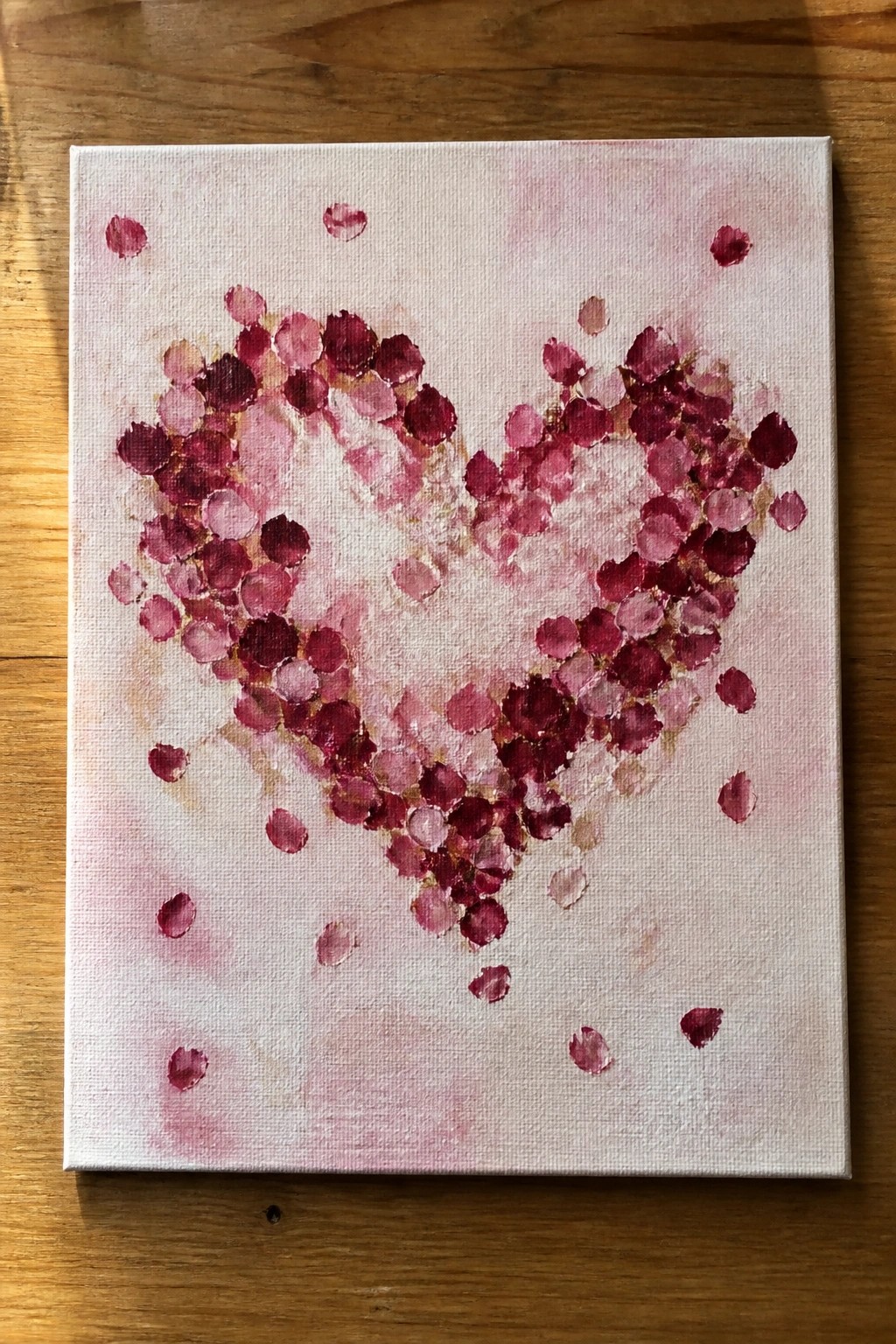 Pink and red dotted heart painting on canvas atop wooden table