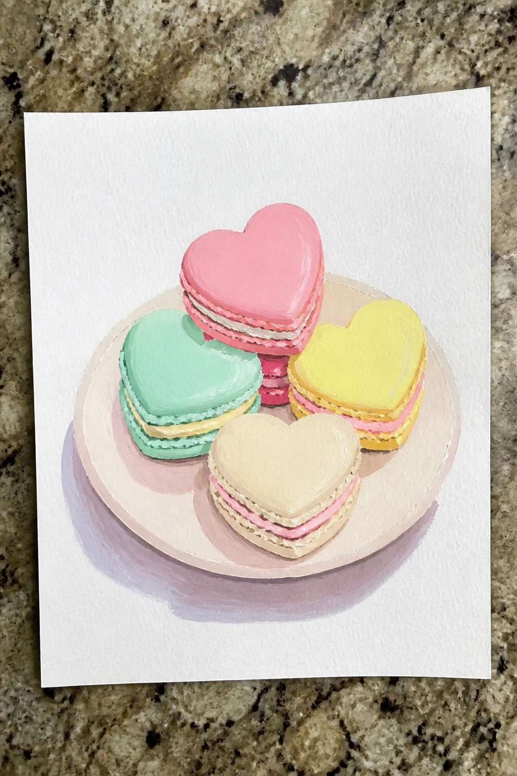 Four colorful heart-shaped macarons on a pink plate atop marble surface