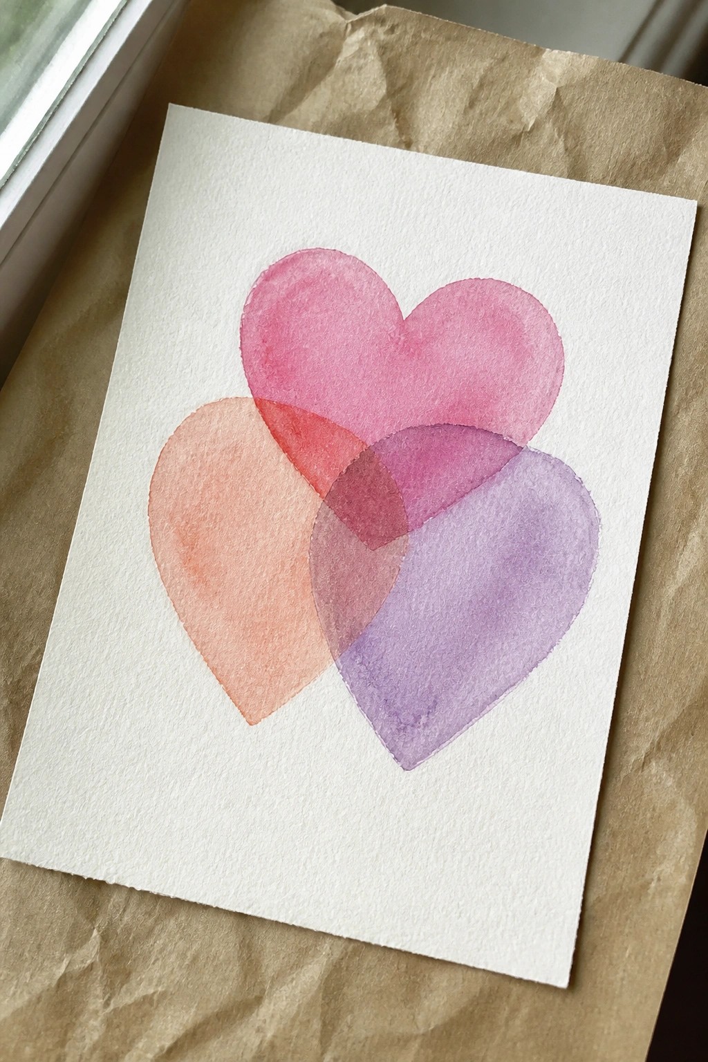 Three overlapping watercolor hearts in pink, orange, and purple on white paper.