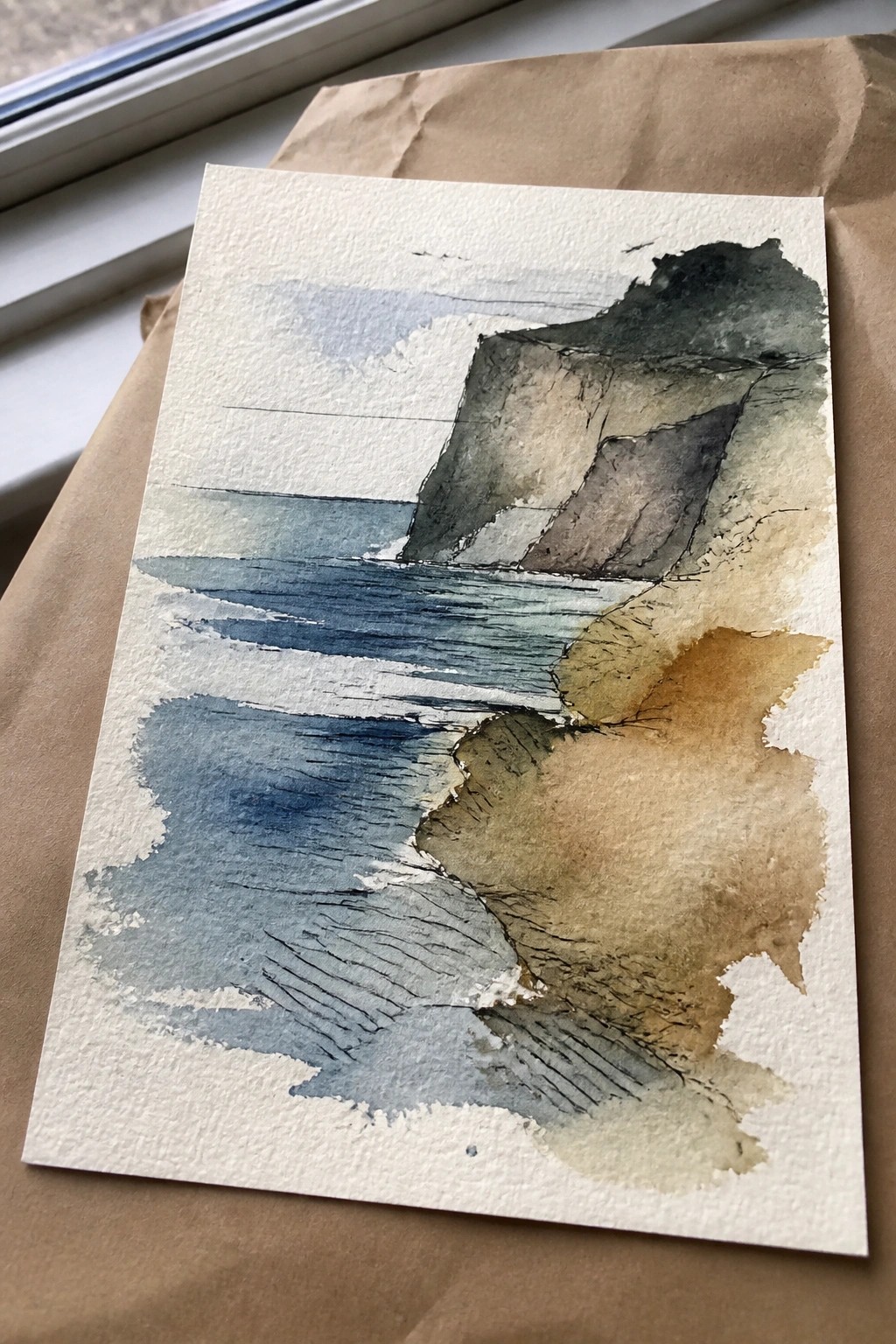 Watercolor seascape of cliffs and blue ocean waves on white paper over brown bag