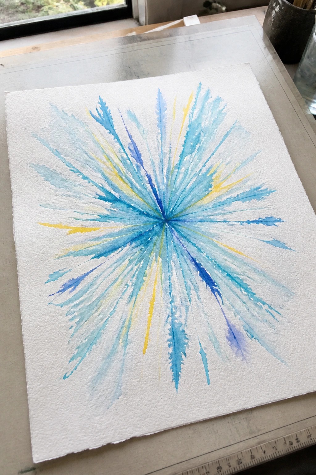 Watercolor starburst with blue turquoise and yellow rays on white paper