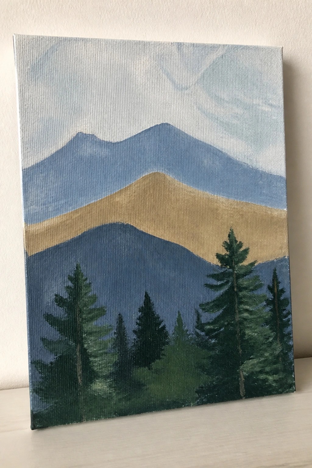 Landscape painting of blue mountains with green pine trees under cloudy sky