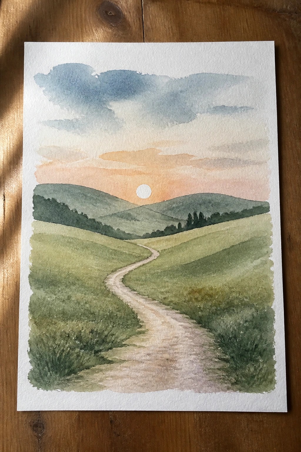 Watercolor of winding path through rolling green hills under orange sunset sky.