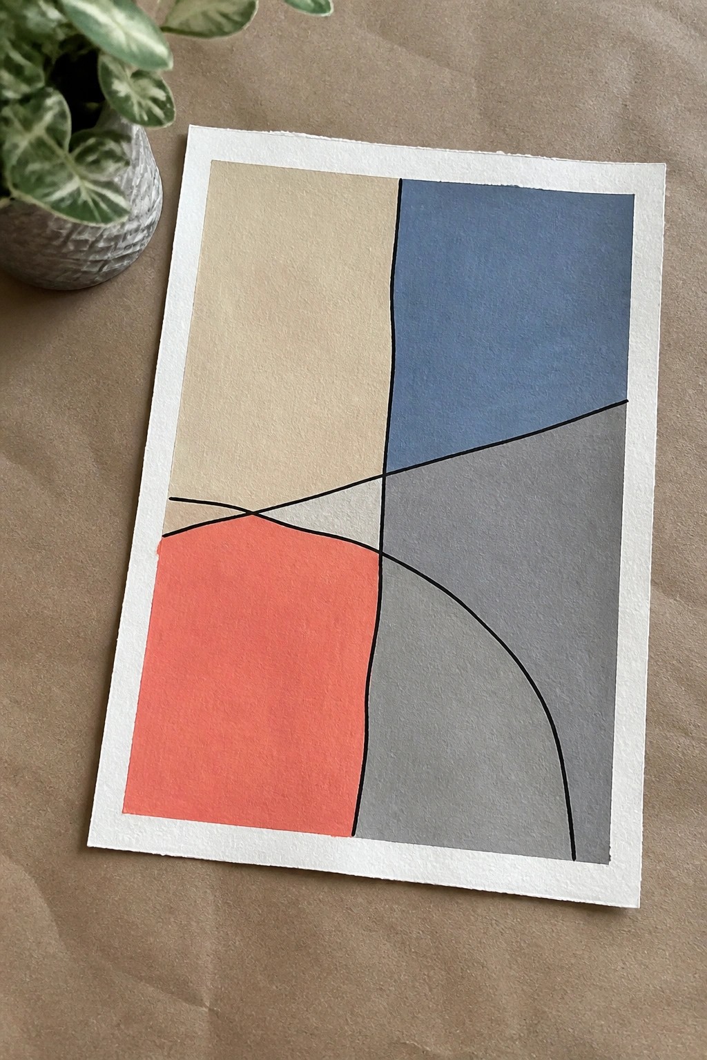 Abstract geometric artwork with beige, blue, gray, and coral sections beside a potted plant.