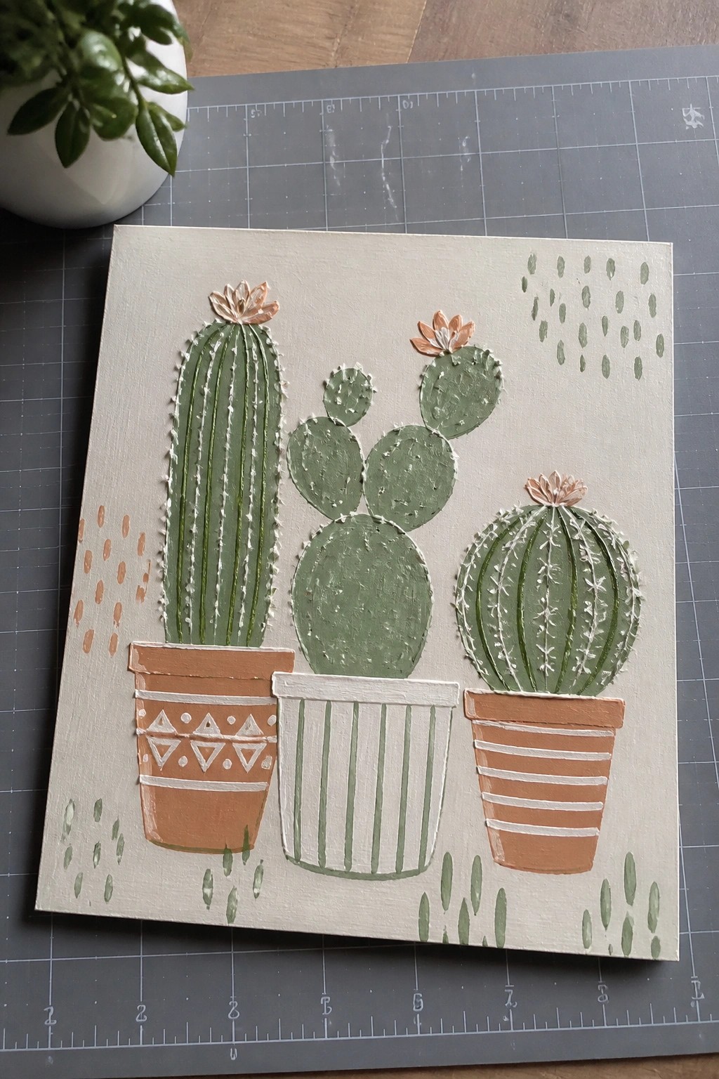 A square canvas painting of three potted cacti with raised white lines on the plants and patterned pots against a light background with scattered dots.