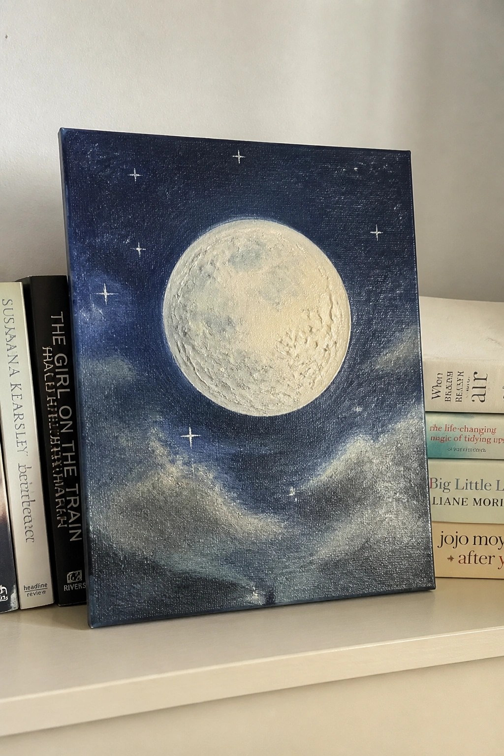 Large textured moon painting in starry blue sky on shelf with books