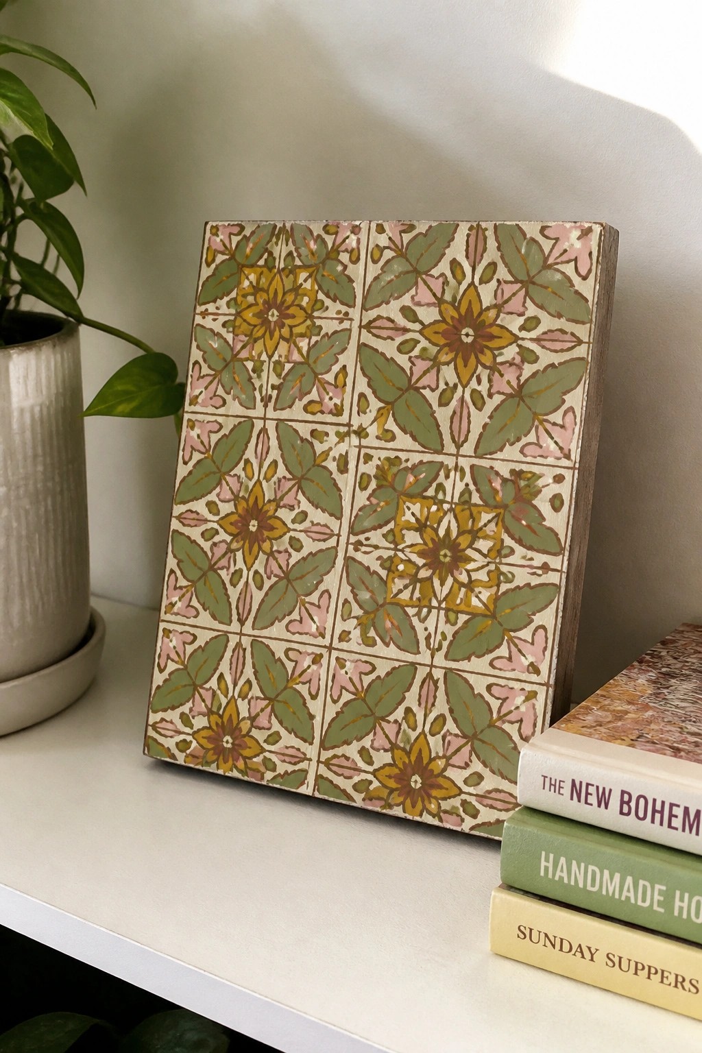 Floral patterned wooden tile panel beside stacked books and potted plant