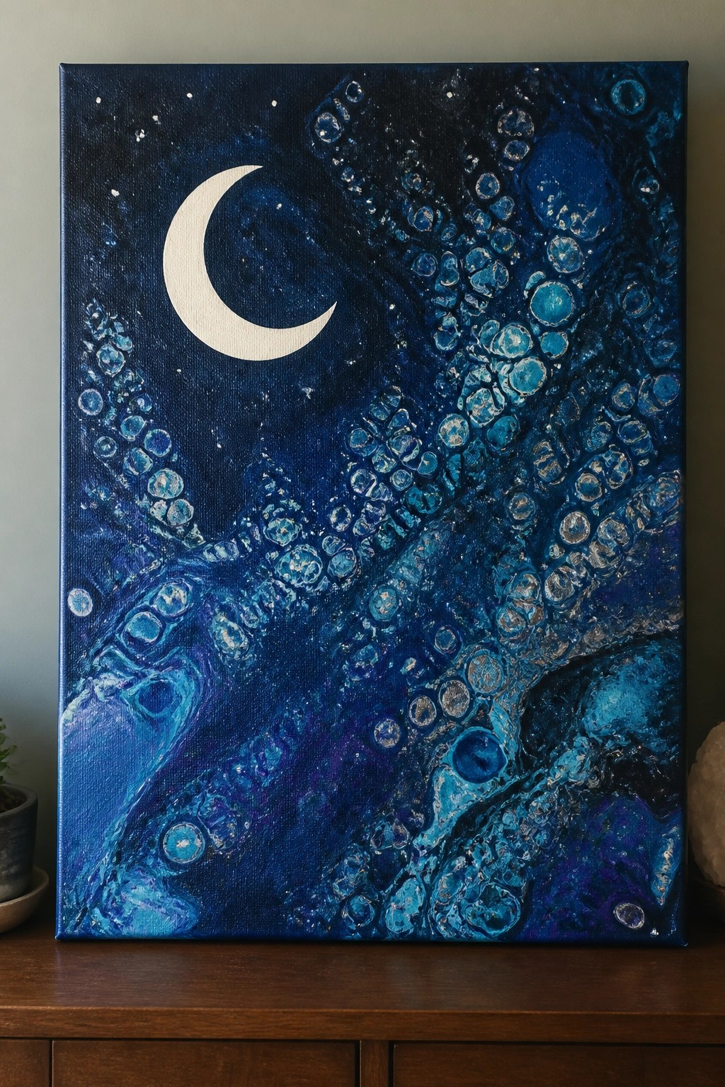 Textured painting of white crescent moon above swirling blue octopus tentacles with suckers.