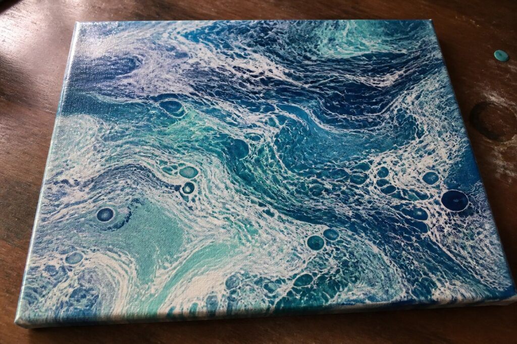 Abstract fluid art canvas with swirling blues, greens, and bubbles on wood.