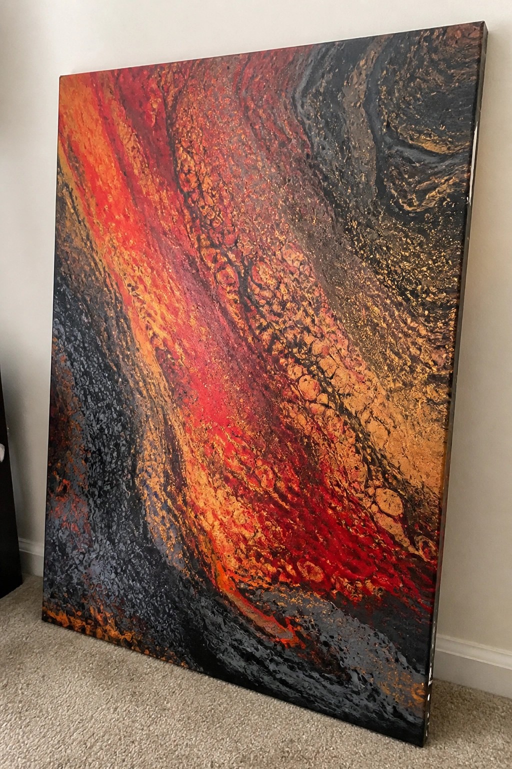 Large abstract painting with swirling red, orange, black, and gold textures leaning on wall